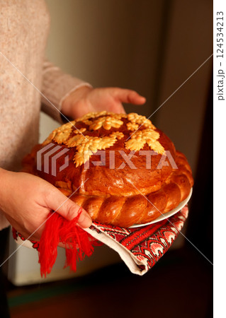 A traditional Ukrainian korovai held in hands, symbolizing celebration and hospitality. The beautifully decorated bread features intricate dough patterns, often with wheat motifs A traditional Ukrainian korovai held in hands, symbolizing celebration and hospitality. The beautifully decorated bread features intricate dough patterns, often with wheat motifs 124534213