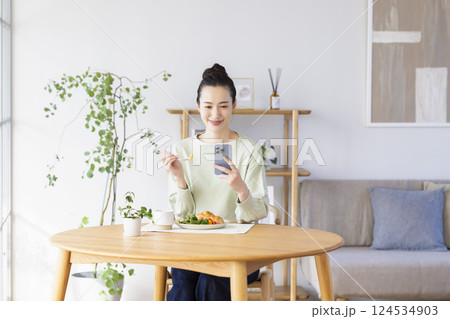 スマホを見ながら食事をとる女性 124534903