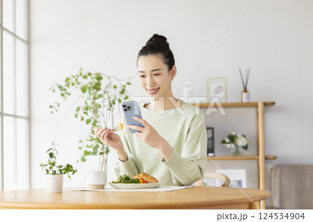 スマホを見ながら食事をとる女性 スマホを見ながら食事をとる女性 124534904