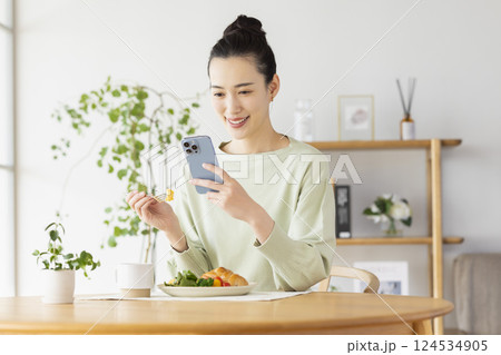 スマホを見ながら食事をとる女性 124534905