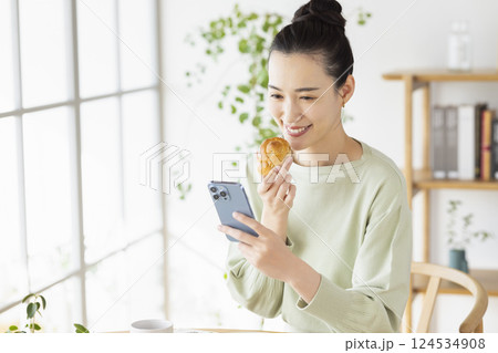 スマホを見ながら食事をとる女性 124534908