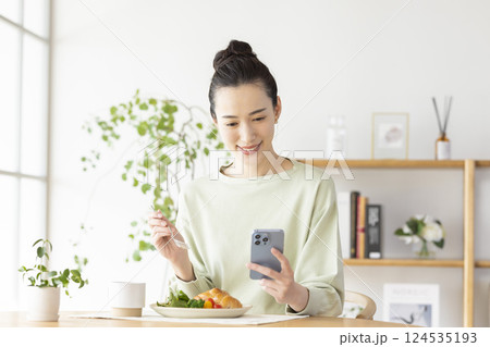 スマホを見ながら食事をとる女性 124535193