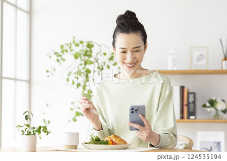 スマホを見ながら食事をとる女性 スマホを見ながら食事をとる女性 124535194