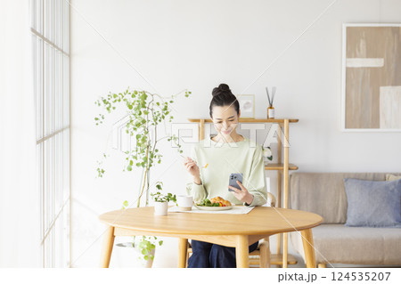 スマホを見ながら食事をとる女性 スマホを見ながら食事をとる女性 124535207