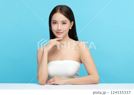 A beautiful young Asian woman with clean, fresh skin against a blue background. Skincare, facial treatment, cosmetology, beauty, and spa. An elegant portrait of an Asian woman. 124535337