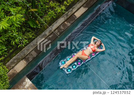 Enjoying sunbathing. Tropical vacation concept. Top view of young woman on inflatable mattress in swimming pool with palm trees. 124537032
