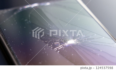 A cracked phone screen with a small light shining through the crack 124537598