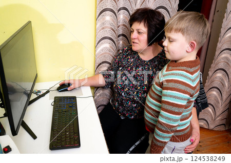Curious boy watches closely as playful adult navigates the colorful screen in a cozy room filled with warmth and laughter during a quiet afternoon 124538249