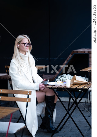 A graceful woman dressed in chic attire savors a peaceful moment of solitude while seated at a charming outdoor cafe on a refreshing cool morning 124538255