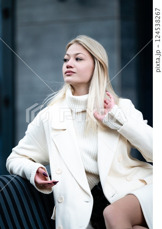 Stylish urban woman with long blonde hair enjoys a moment of relaxation while checking her phone on a modern city street during a bright winter day 124538267