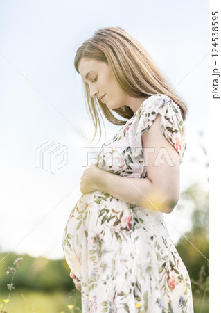 Portrait of beautiful pregnant woman in white summer dress relaxing in meadow full of yellow blooming flowers. Concept of healthy maternity care. 124538595