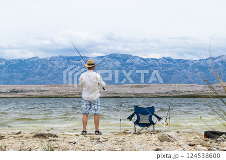 Rear view of old unrecognizable fisherman wearing a straw hat, holding a fishing pole 124538600