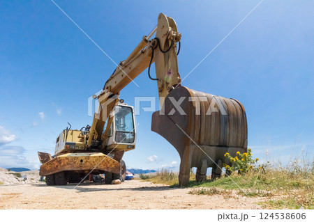 Low angle photo of large excavator on construction site on a sunny day with blue sky. Low angle photo of large excavator on construction site on a sunny day with blue sky. 124538606