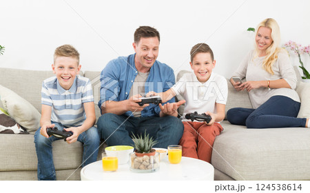 Happy young family playing videogame console on TV. Spending quality leisure time with children and family concept. Gaming consoles are generic and debranded. 124538614