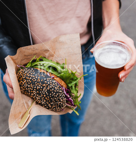 Close up of woman hands holding delicious organic salmon vegetarian burger and homebrewed IPA beer on open air beer an burger urban street food festival in Ljubljana, Slovenia 124538820