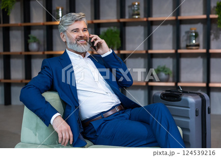 Good-looking well-dressed bearded man sitting in the chair and talking on the phone Good-looking well-dressed bearded man sitting in the chair and talking on the phone 124539216