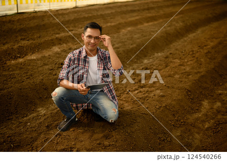 Agronomist holding a laptop and checking soil quality in an agricultural Agronomist holding a laptop and checking soil quality in an agricultural 124540266