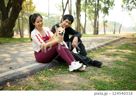 Happy young couple sitting on the curbside with their dog, resting after a workout in a sunny park 124540318