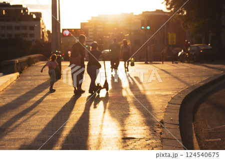 Abstract urban scene. Silhouettes of people in the warm light walking along a street at sunset. Long shadows on a ground. Sun setting dawn. 124540675