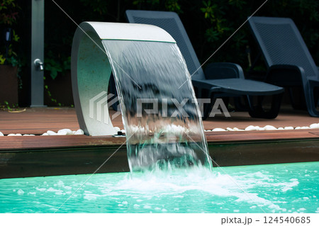 Swimming pool with artificial waterfall in backyard of a luxury hotel on the tropics. Summertime vacation. Wooden floor near pool with blue water.  124540685