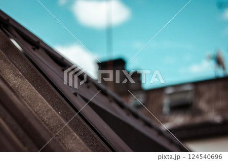 Covering of a tiled brown roof shingles against blue sky. Metal roofing construction abstract photo with selective focus. Housing, real estate concept 124540696