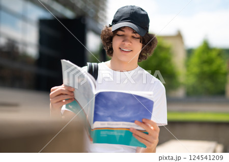 Young university student wearing backpack walking on campus and reading book 124541209