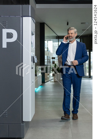 Good-looking tall caucasian man in a nice suit talking on the phone in the business center corridor 124541624