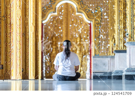 Asian Man meditates on the ground with reflection in the sunlight pouring into the temple church with gold gold Thai pattern blur background. Asian Man meditates on the ground with reflection in the sunlight pouring into the temple church with gold gold Thai pattern blur background. 124541709