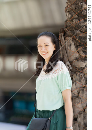Aa Asian stylish woman with long hair and green blue dress is standing there pleasantly grinning. Aa Asian stylish woman with long hair and green blue dress is standing there pleasantly grinning. 124541741
