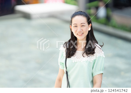 Aa Asian stylish woman with long hair and green blue dress is standing there pleasantly grinning. Aa Asian stylish woman with long hair and green blue dress is standing there pleasantly grinning. 124541742