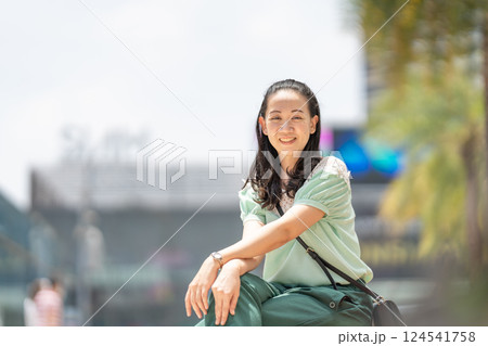 Aa Asian stylish woman with long hair and green blue dress is sitting there pleasantly grinning. Aa Asian stylish woman with long hair and green blue dress is sitting there pleasantly grinning. 124541758