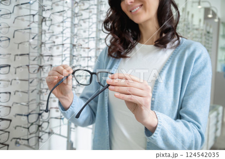 Female customer choosing new glasses in optic shop and looking enjoyed Female customer choosing new glasses in optic shop and looking enjoyed 124542035