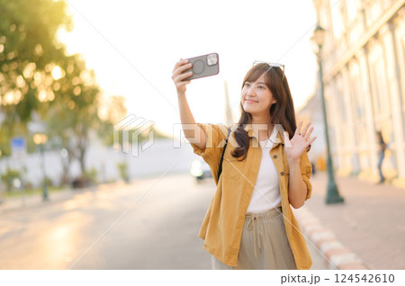 Traveler asian woman in her 30s making a livestream and selfie with a smartphone enjoying travel in Bangkok, Thailand. Journey trip lifestyle, world travel explorer or Asia summer tourism concept. Traveler asian woman in her 30s making a livestream and selfie with a smartphone enjoying travel in Bangkok, Thailand. Journey trip lifestyle, world travel explorer or Asia summer tourism concept. 124542610