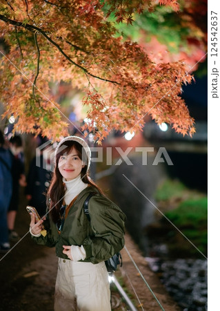 Asian woman in a fashionable jacket enjoys the beauty of urban nightfall in Japan. A festive portrait capturing Christmas cheer and snowy delight. 124542637