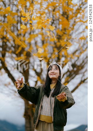 Asian woman enjoys a leisurely walk amid vibrant ginkgo leaves. A casual and refreshing portrait capturing the beauty of fall in Japan. 124542638