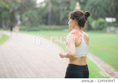 Shoulder pain problem. woman jogger. 30s asian female wearing white sportswear holding her shoulder with pain after running exercise in public park. Shoulder pain problem. woman jogger. 30s asian female wearing white sportswear holding her shoulder with pain after running exercise in public park. 124542647