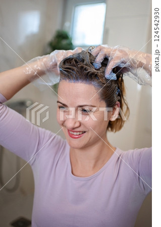 Woman applying purple hair dye at home in the bathroom Woman applying purple hair dye at home in the bathroom 124542930