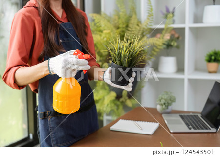 Plant Care and Preparation. A woman sprays a plant while taking care of an indoor gardening setup. Plant Care and Preparation. A woman sprays a plant while taking care of an indoor gardening setup. 124543501