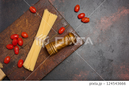 Uncooked spaghetti pasta tied with twine, cherry tomatoes, and a wooden pepper grinder on a rustic wooden cutting board Uncooked spaghetti pasta tied with twine, cherry tomatoes, and a wooden pepper grinder on a rustic wooden cutting board 124543666