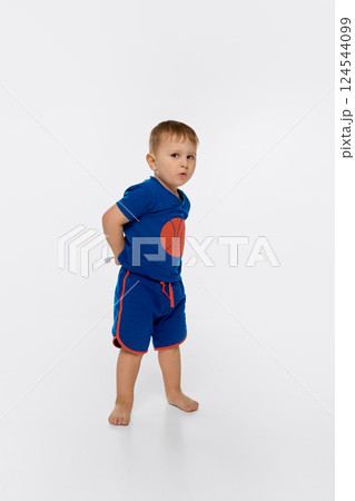 Child standing with toothbrush behind back, looking sideways with playful face isolated on white background. 124544099