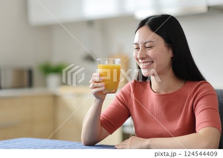 Happy asian woman drinking orange juice in the kitchen Happy asian woman drinking orange juice in the kitchen 124544409