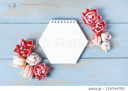 Open paper notebook with empty page with pink and white tulips on wooden blue background. Top view, flat lay, work space on purple background. Open paper notebook with empty page with pink and white tulips on wooden blue background. Top view, flat lay, work space on purple background. 124544763