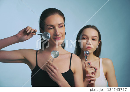Two women using facial tools for skincare in a studio setting Two women using facial tools for skincare in a studio setting 124545737