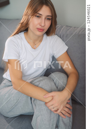 Young woman post-traumatic stress disorder experiencing headache while sitting depression on a couch in a modern living room home during daytime vertical photo 124546021