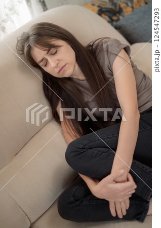 Young woman post-traumatic stress disorder experiencing headache while sitting depression on a couch in a modern living room home during daytime suffers from a psychological disorder, syndrome 124547293