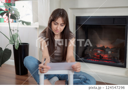 Young lady is seated at a kitchen table, attentively using a pen to write on a piece of paper writes a letter 124547296