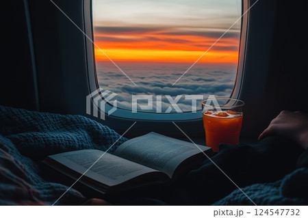 Cozy Airplane Seat with Blanket, Book, and Drink at Sunset Above Clouds 124547732