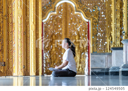 Asian Man meditates on the ground with reflection in the sunlight pouring into the temple church with gold gold Thai pattern blur background. 124549505