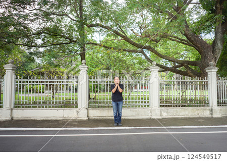 Asian Black T-Shirt is standing in front of white vintage fence beside the road in the afternoon time. 124549517