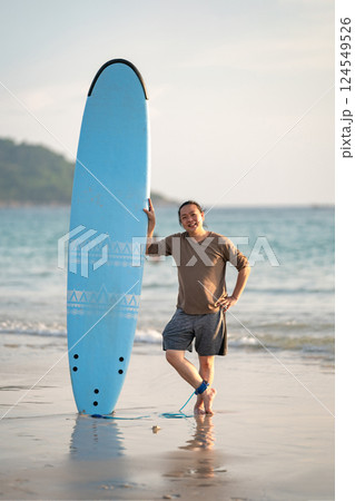 Smart Asian Man long hair touches and poses with Standed Surfboard on the beach in Twilight time 124549526